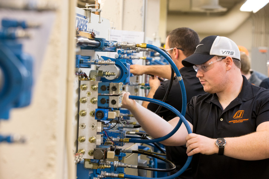 a mechanical engineering technology student moves large hoses on a panel of hook ups in a lab.