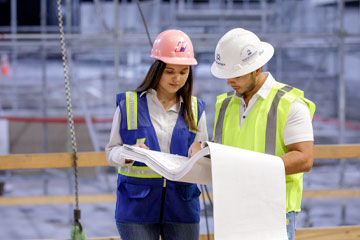 Two OSU student wearing construction hats and safety vests looking at a set on plans on a construction site.