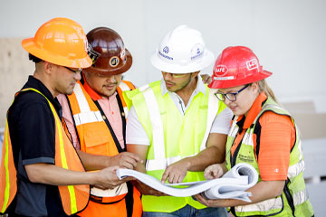 4 OSU Students wearing construction hats and safety vests, gathered around construction plans.